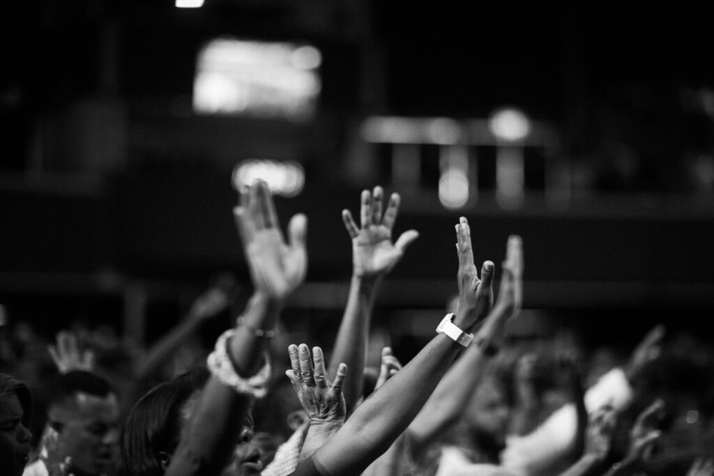 A group of people raising hands in a black and white concert setting, showing unity and celebration.